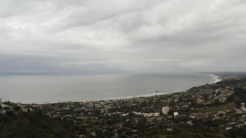 Large statue of cross occupies mountain top with city sprawled below next to the ocean