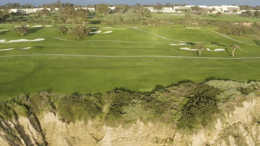 A lush green golf course on a coastal cliff on a sunny day