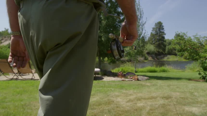 A man carrying a fishing pole as he walks through a backyard towards a lake
