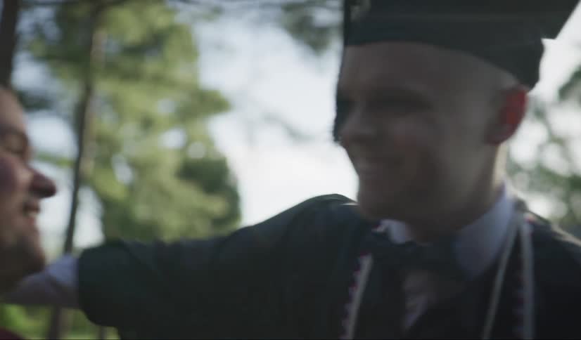 A young man in graduation attire hugs his father