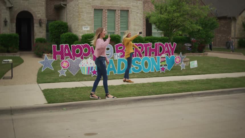 As girl stands in yard near birthday sign friends and family drive by to celebrate at a social distance