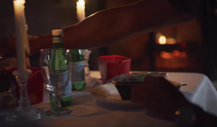 A black man and woman eat Chinese takeout on a table set for dinner on the back patio at dusk.