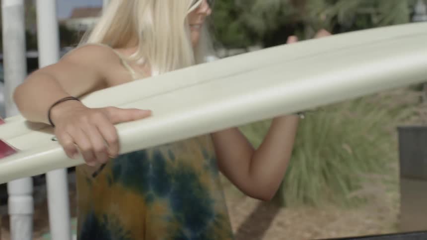 A woman approaches the bed of a pick up truck to lift her surfboard and carry it away