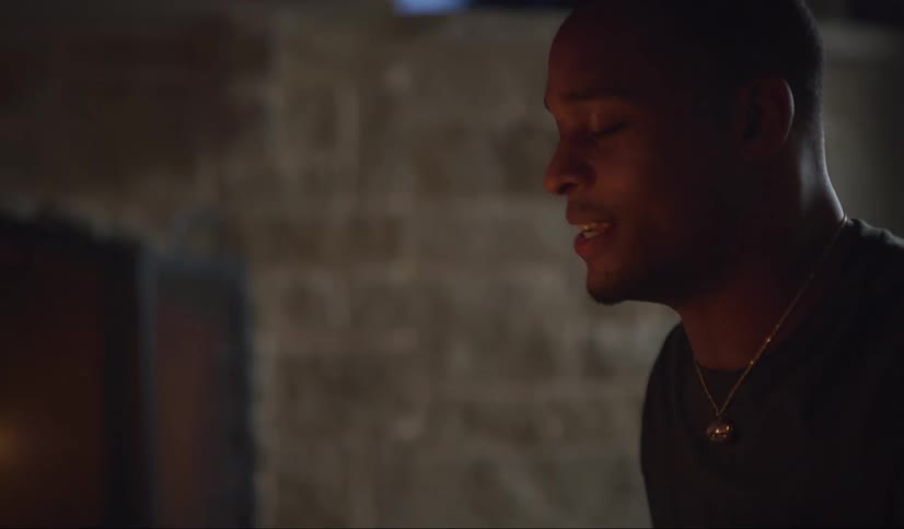 A black man sits smiling laughing and talking outside by the fireplace at night