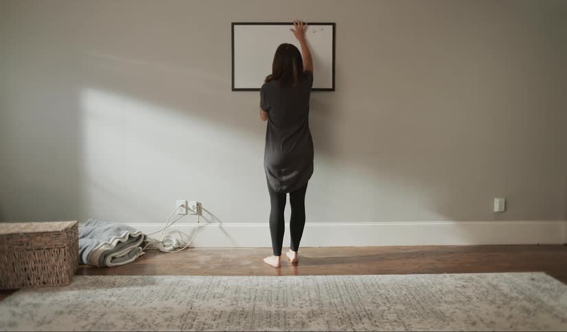 A white woman hangs a frame on the wall of her home