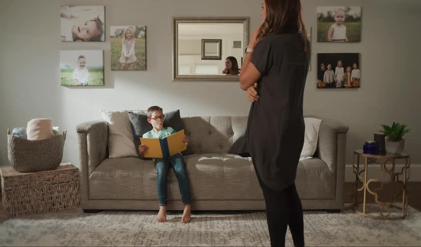 A woman walks into the living room with her son sitting on the couch