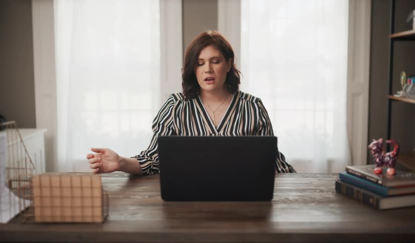 Woman sits at a home office desk with a laptop on a Zoom call.