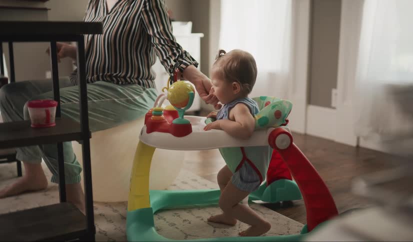 A mom, wearing pajama bottoms on a Zoom call, feeds her baby snacks below the desk.