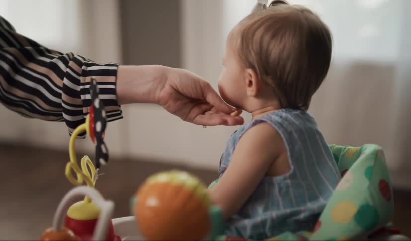 Woman feeds snacks to her baby sitting in a walker toy.