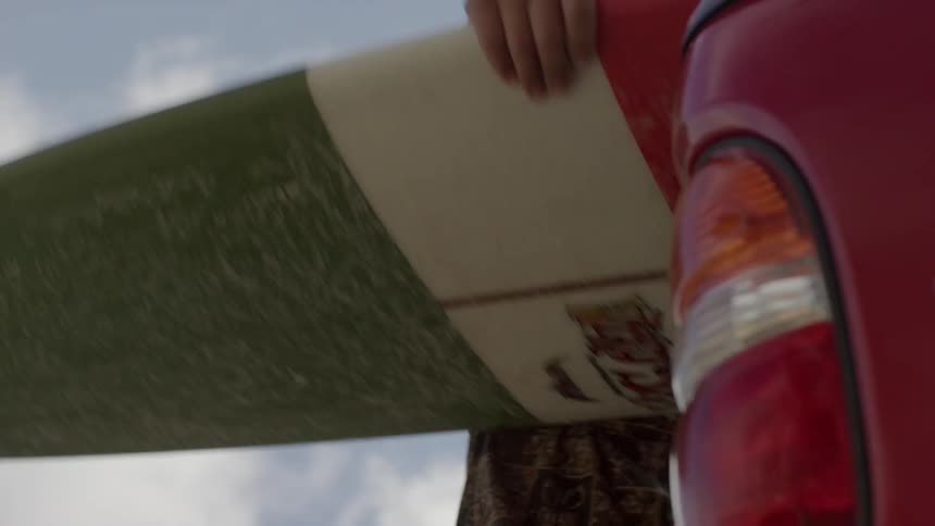 A man removes a surfboard from a pickup bed