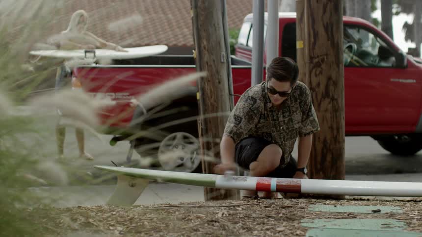 A man is polishing a surfboard by a street