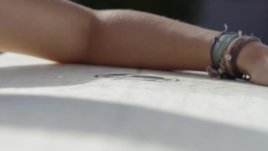 A woman's hand and arms are seen waxing a surfboard