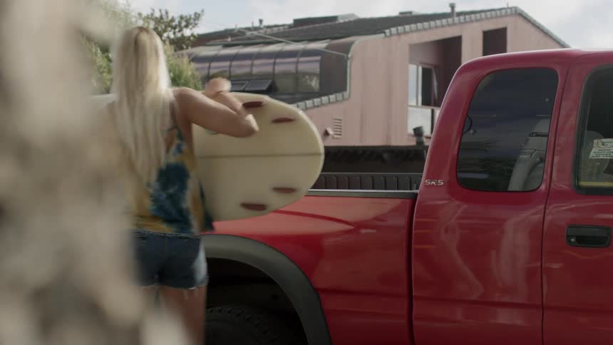 A young woman lifts a surfboard out of the bed of a pickup truck