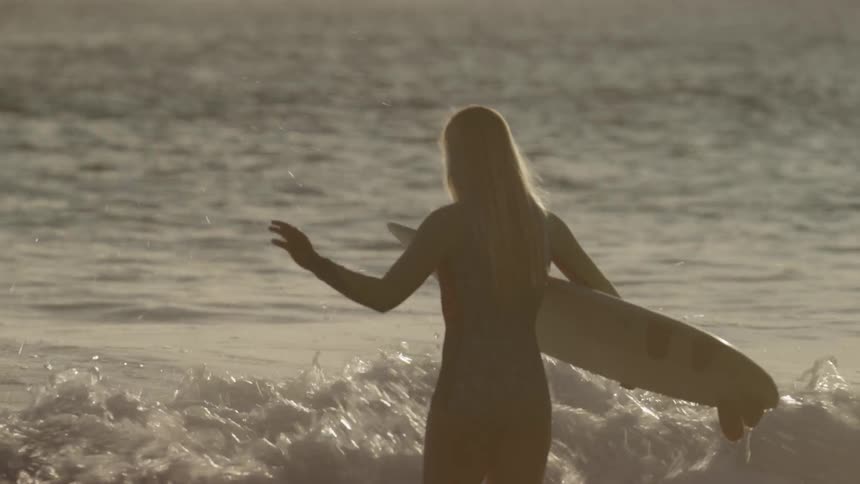 A woman holds a surfboard and waits for the tide to come in