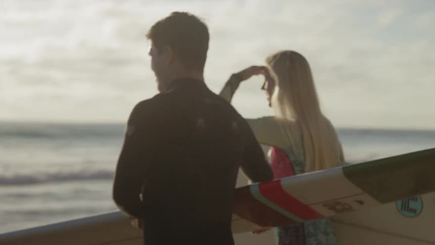 A man and woman holding surfboards walk towards the ocean