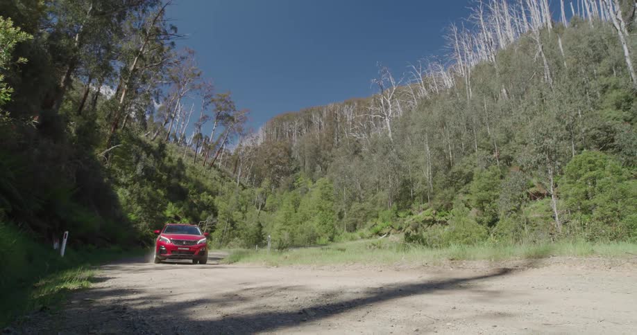 A red crossover vehicle drives down a curved dirt road in slow motion
