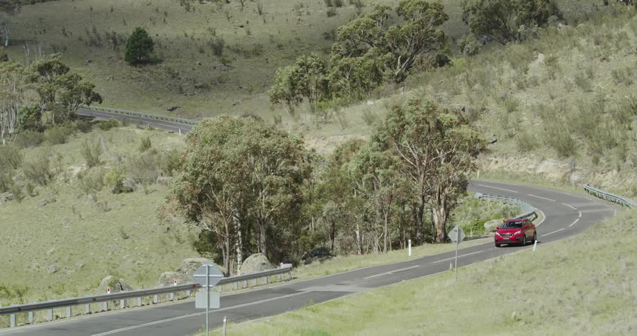 Red car drives along curvy road on sloping terrain