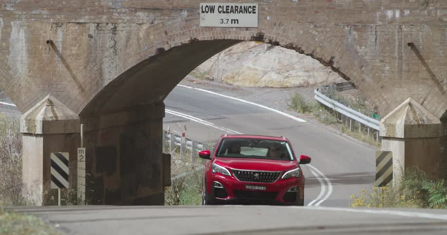 Man drives the red car on the highway under the bridge