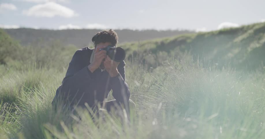 A photographer crouching in tall grass while preparing to take a photo