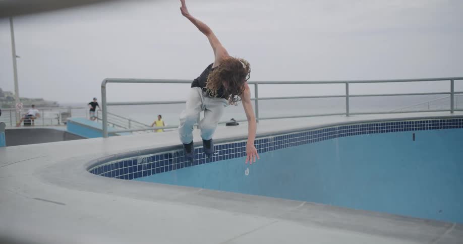 A teenager rollerblades in an empty swimming pool in a public park