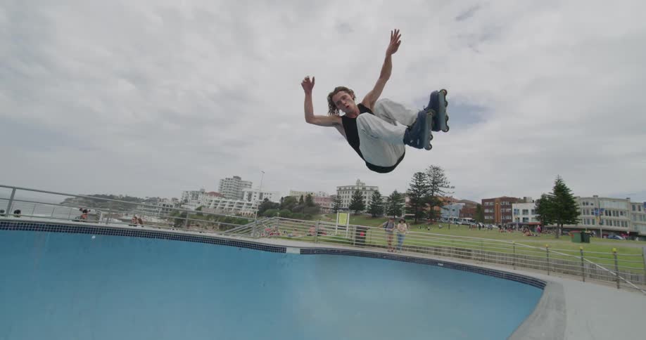 A man inline skating doing tricks in a skate park with two people in the background looking on