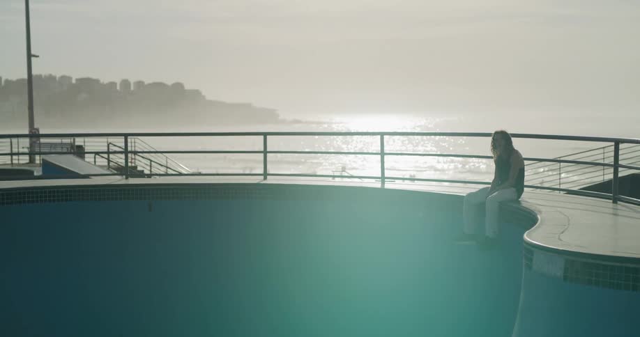 A man is sitting on the edge of an empty pool