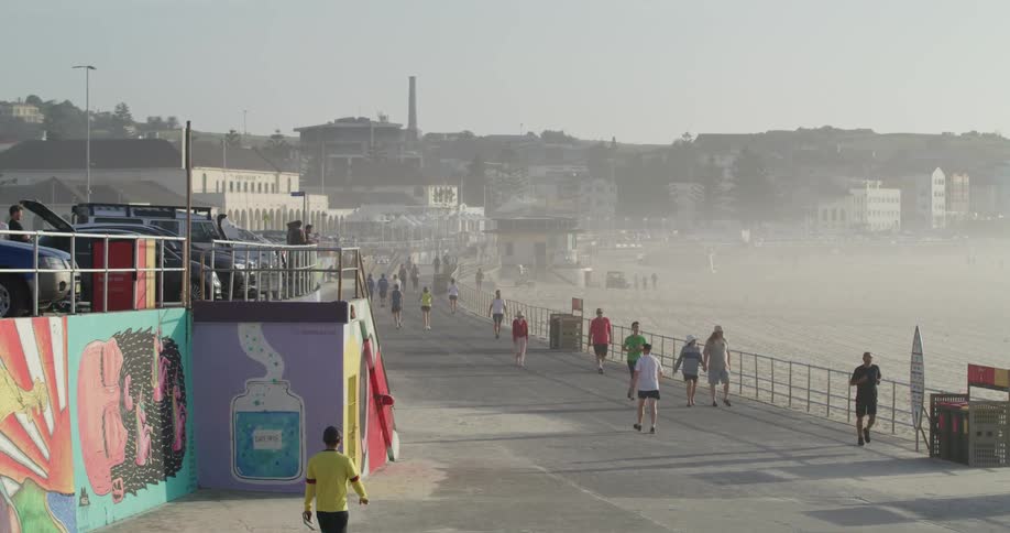 People move along boardwalk near city as fog shrouds beach