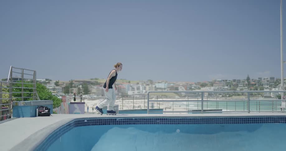 A teenager rollerblades in an empty pool in a public park near a city neighborhood