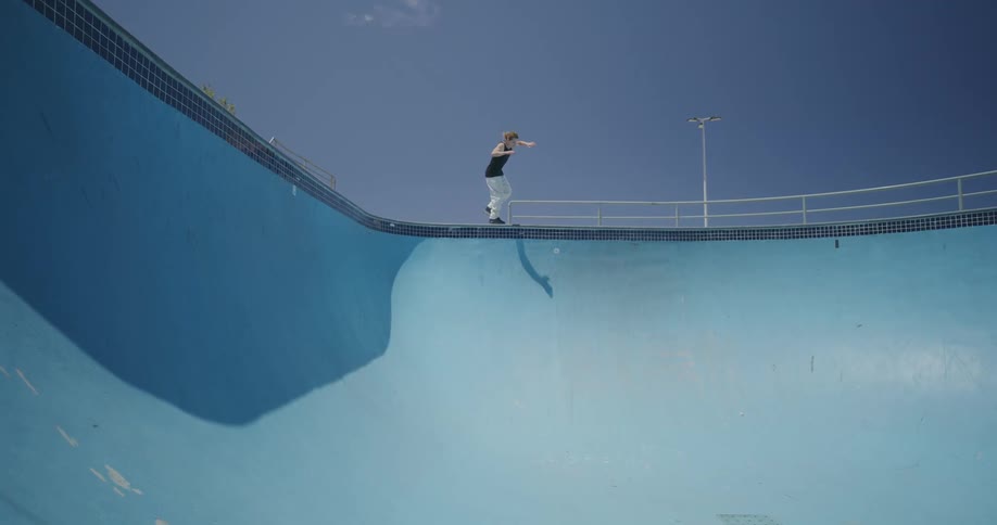 A young man skates an empty swimming pool