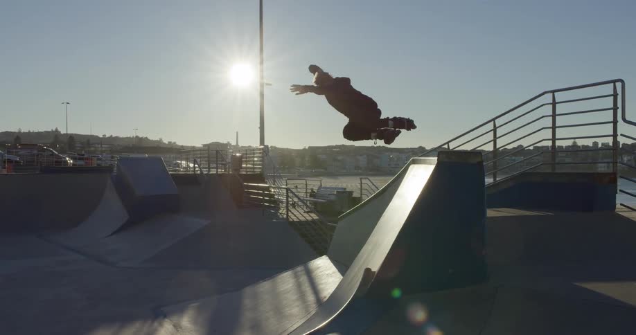 A skater jumping atop a ramp and grinding on it before jumping off and skating down an adjacent ramp