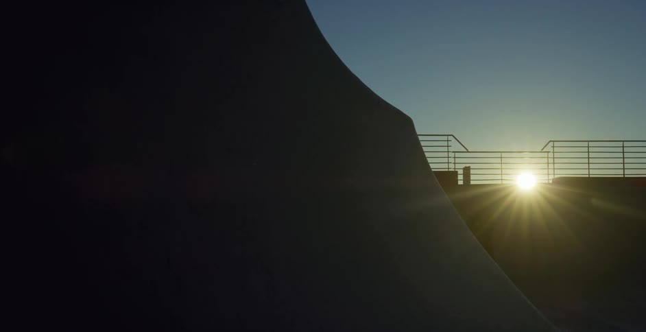 A person is shown in silhouette rollerblading at a park at dusk