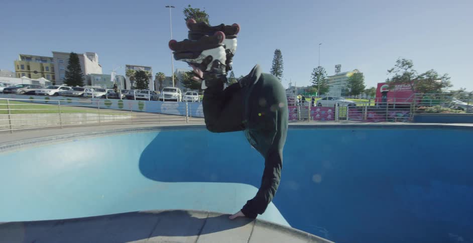 A man rollerblades and does tricks in an empty pool in a skate park on a sunny day