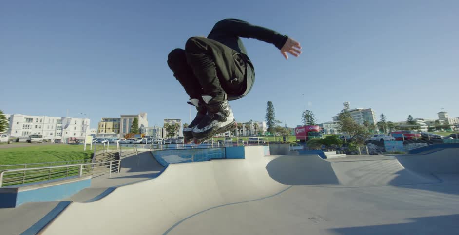 A skater jumping and grinding atop a rail before jumping off and skating down a ramp