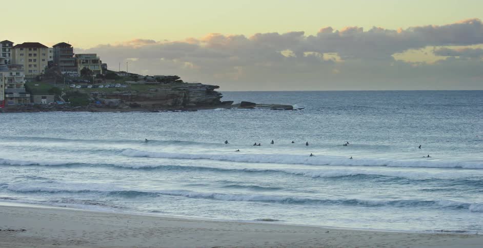 A beach with people in the water with buildings and the sky in the background