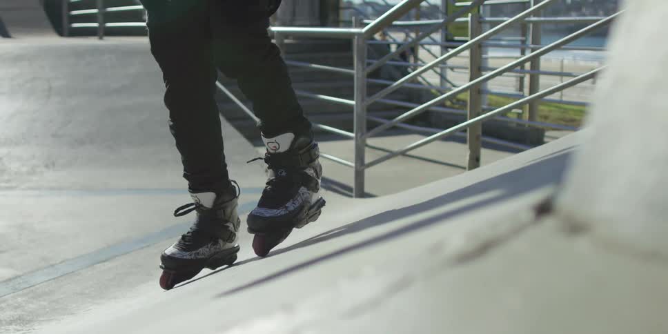 A man wearing roller blades walks up a cement slope at a public park
