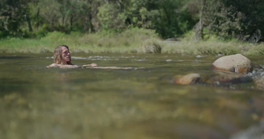 Person floats in river near bank and stones