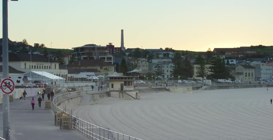 People walking on a boardwalk near the beach with buildings in the background