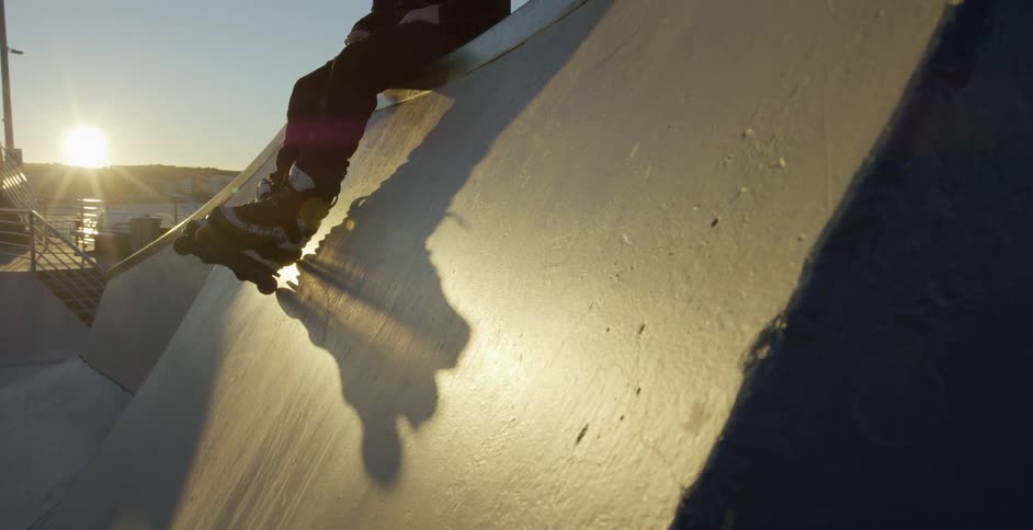 A person with inline skates sitting in a skate park with the sun in the background