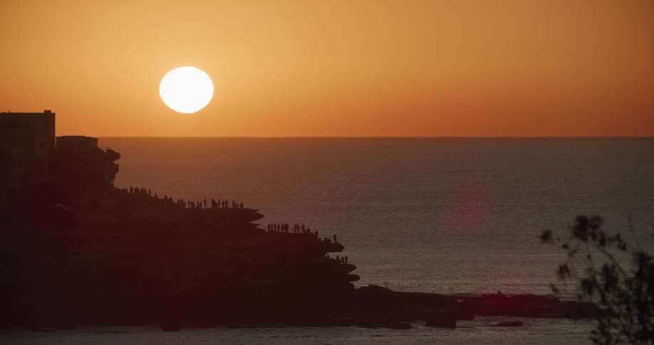 The silhouette of people standing on shore watching the giant glowing sun rise over the ocean