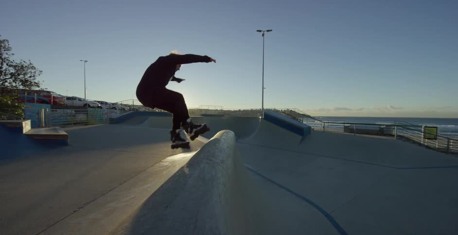 A man roller blades up a ramp in a skate park and does a flip