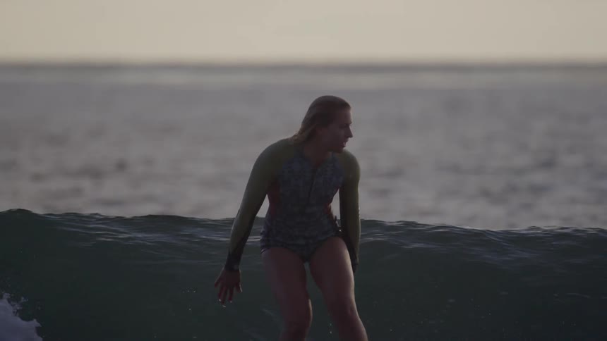 A woman on a surfboard surfing in the ocean at sunset