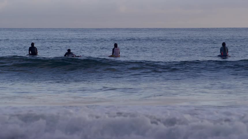 A group of surfers surfing and standing in the ocean with waves at sunset
