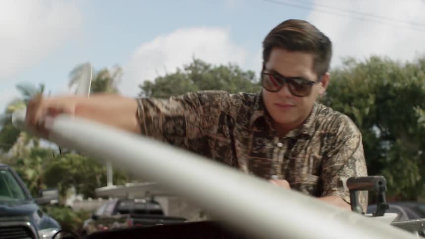 A man removes a surfboard from a rack on a vehicle