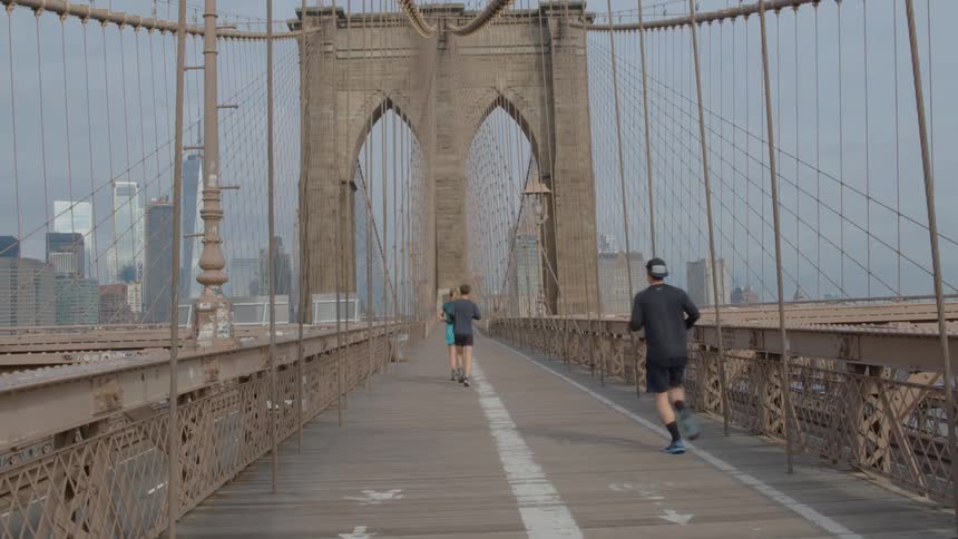 Two men and a woman running on a bridge with buildings in the background