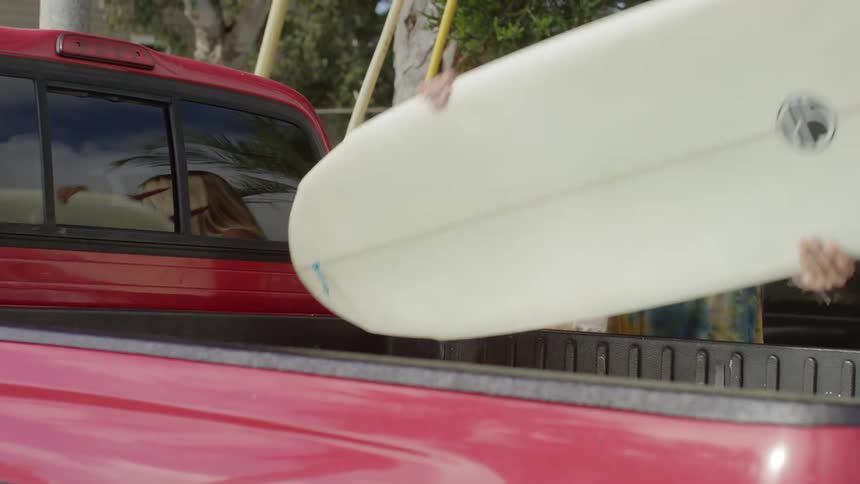 A woman picks up a surfboard from the back of a truck