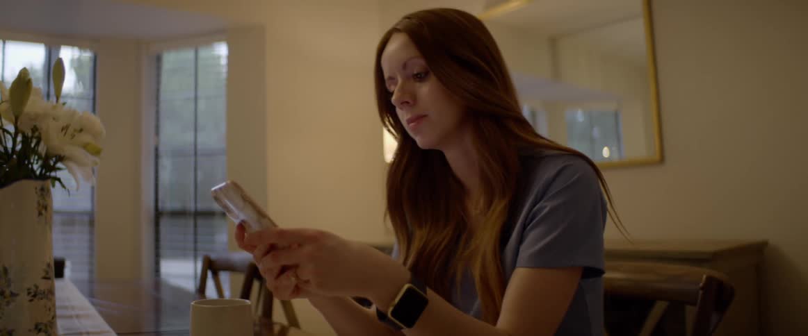 A woman picking up and operating a smartphone while sitting at a table in a house