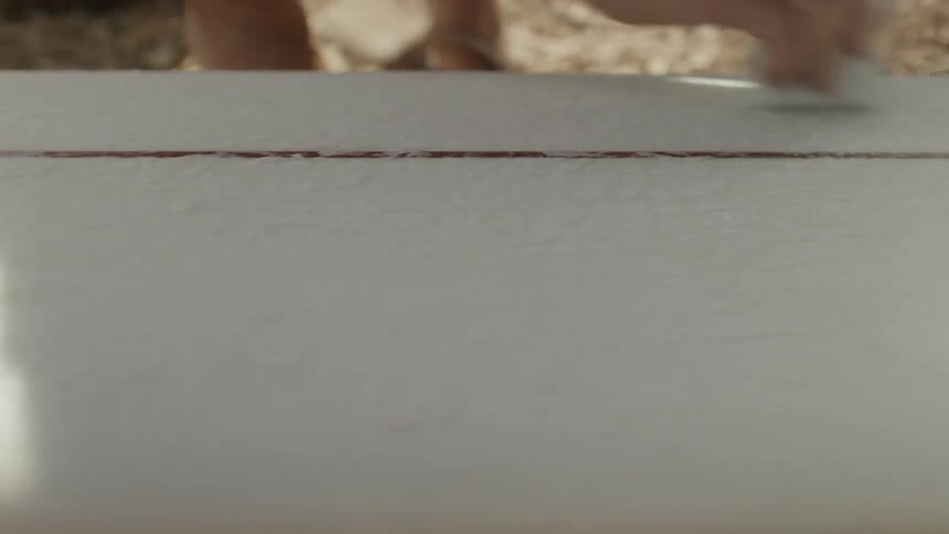 A hand briskly rubs wax over a surfboard