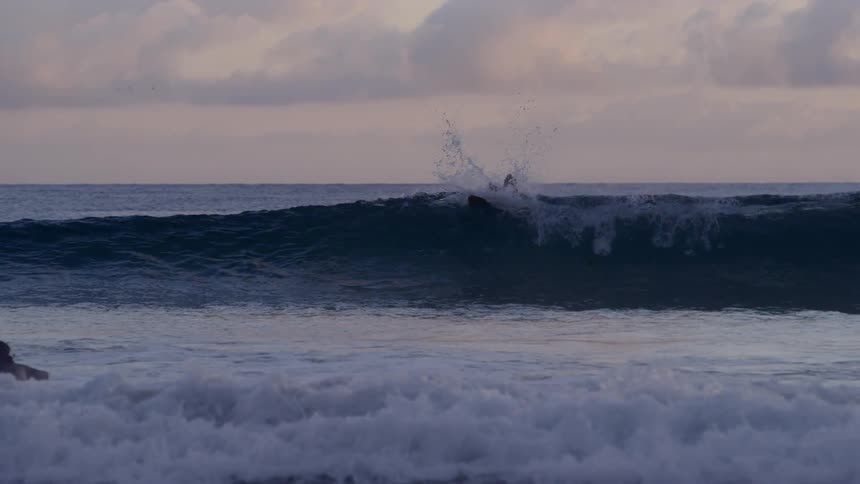 A surfer laying on a surfboard and riding the waves at sunset