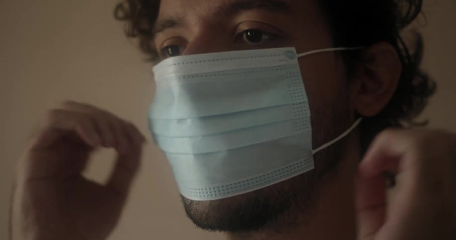 A man putting on a face mask before walking out of frame