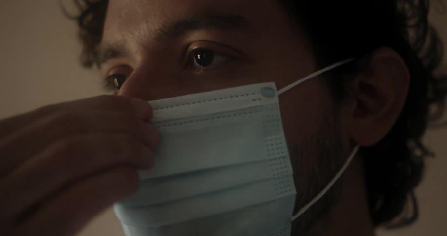 A bearded man putting on a medical face mask
